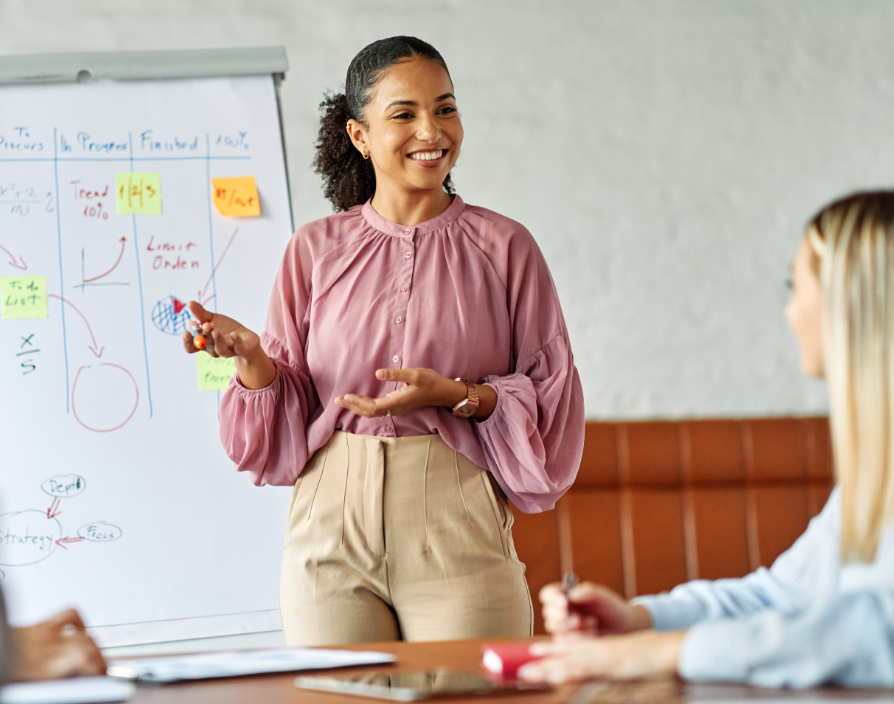 A business leader guiding a team — someone in a suit or smart casual pointing at a whiteboard or strategy plan, while the team executes tasks. This highlights leading vs. doing.